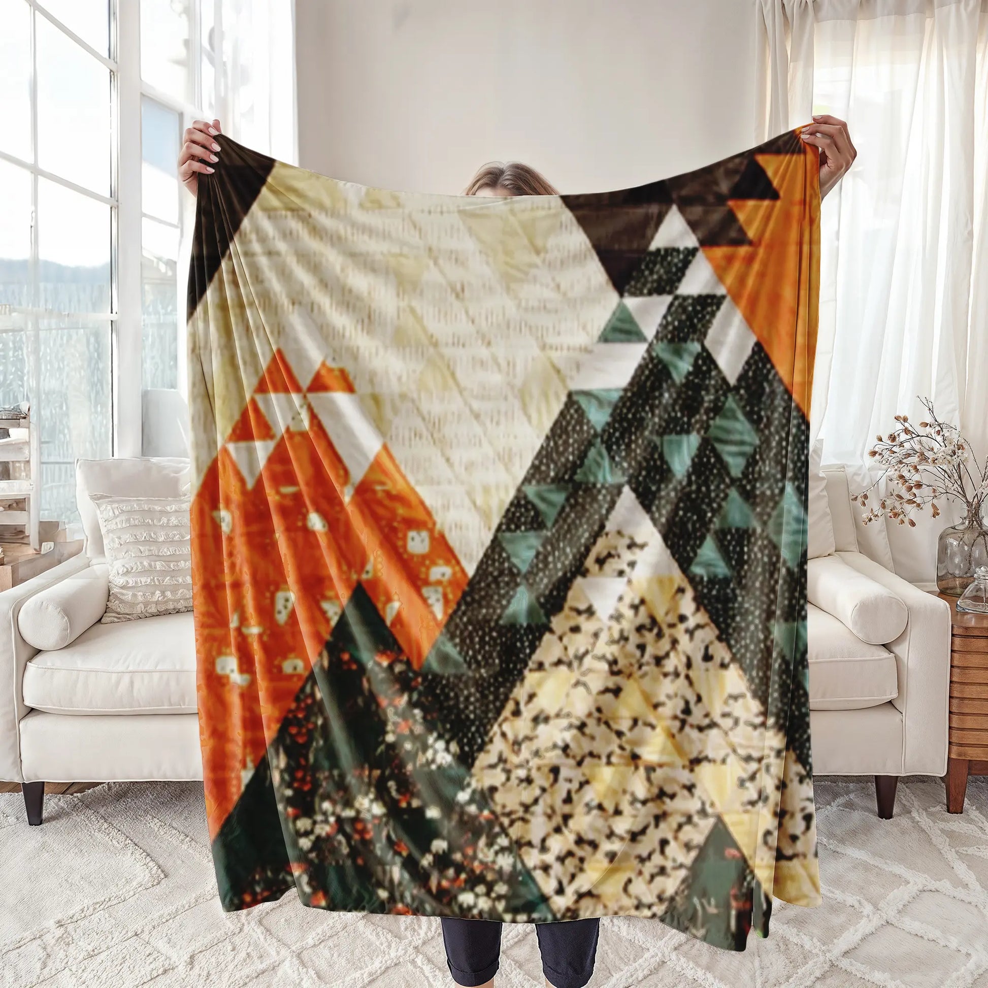 A striking quilt with a geometric mountain-inspired design in bold shades of orange, black, and beige, displayed in a cozy living room